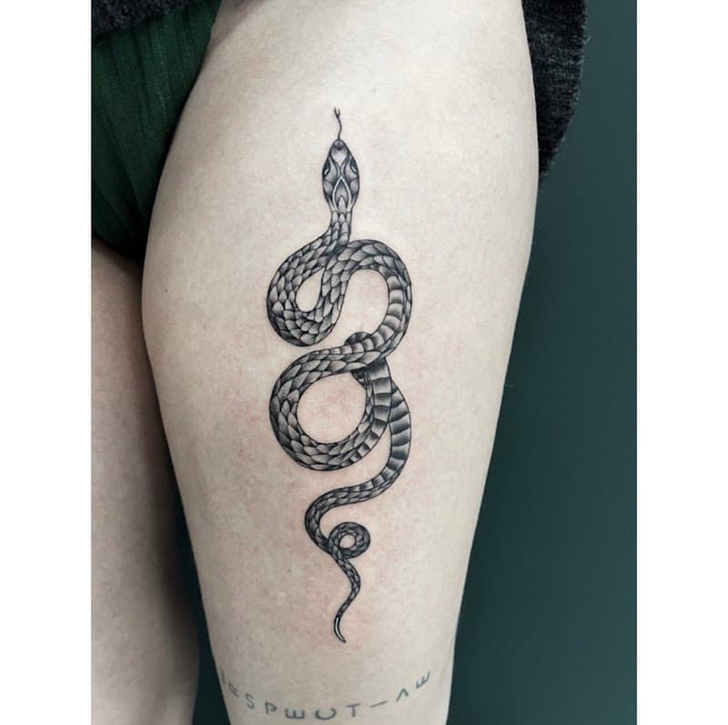 Gedetailleerde zwart-wit slang tattoo op bovenbeen met tekst eronder.