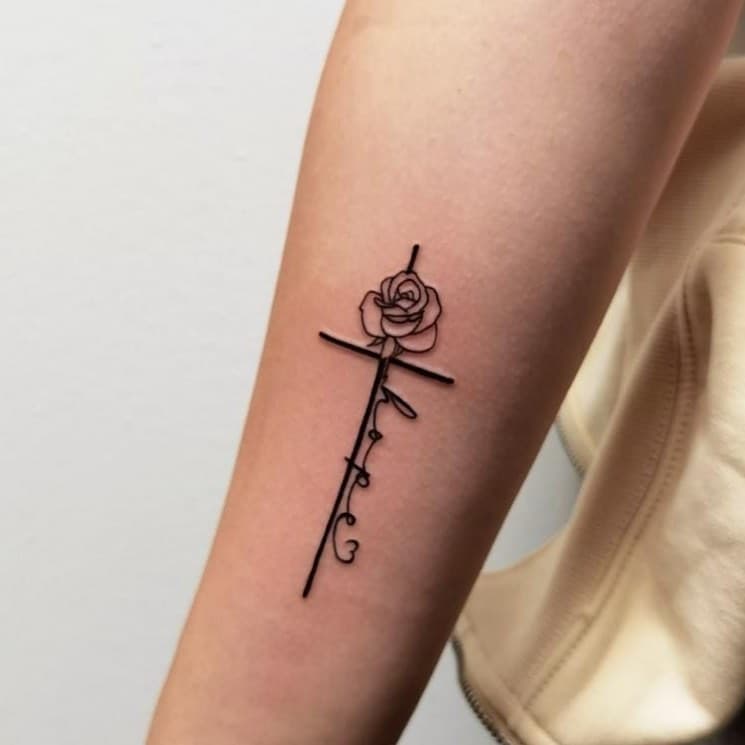 Fineline tattoo van een kruis met een roos en het woord 'hope' op de onderarm.