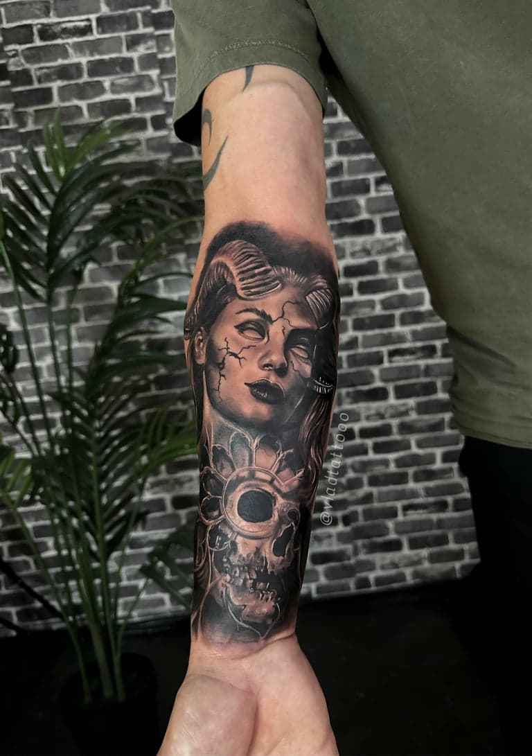 Realistische zwart-wit tattoo van een vrouw met hoorns en een schedel op de onderarm.