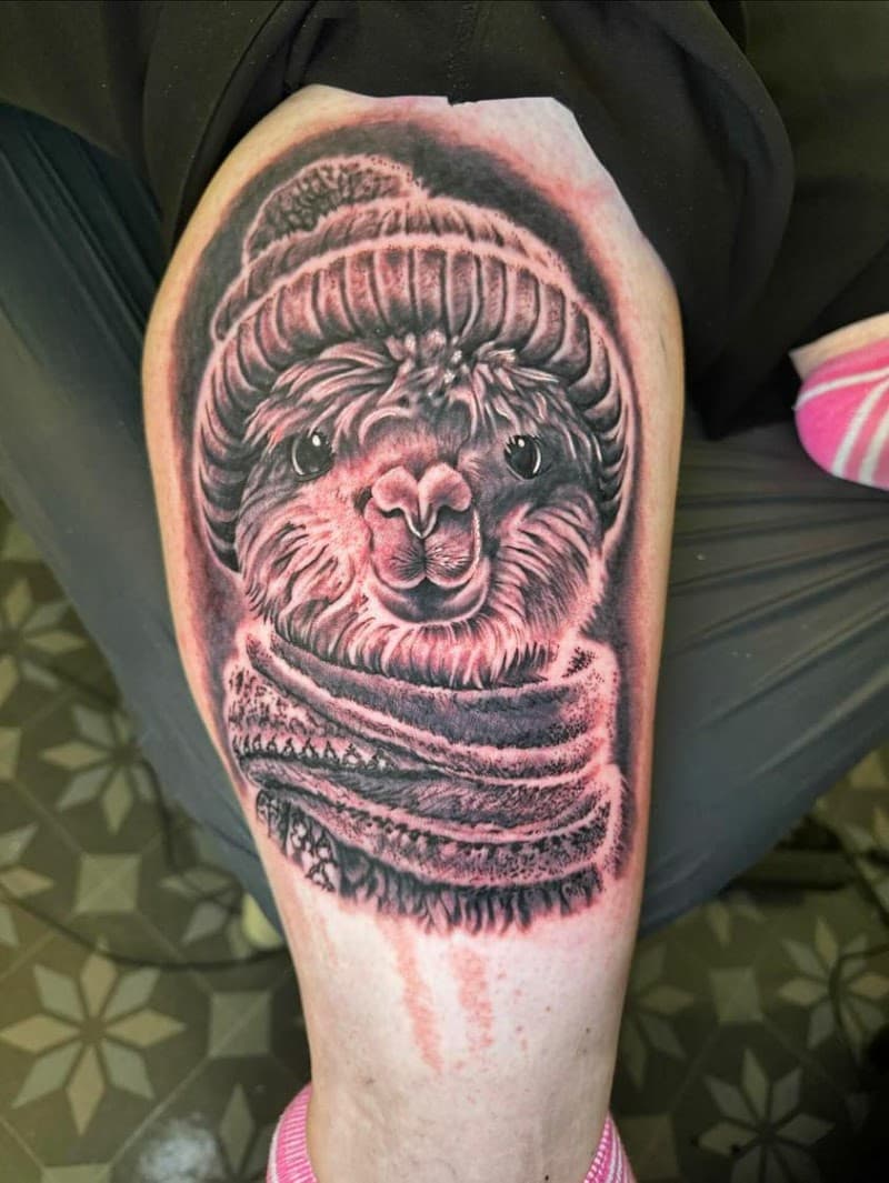 Realistische tattoo van een lama met muts en sjaal op het bovenbeen.