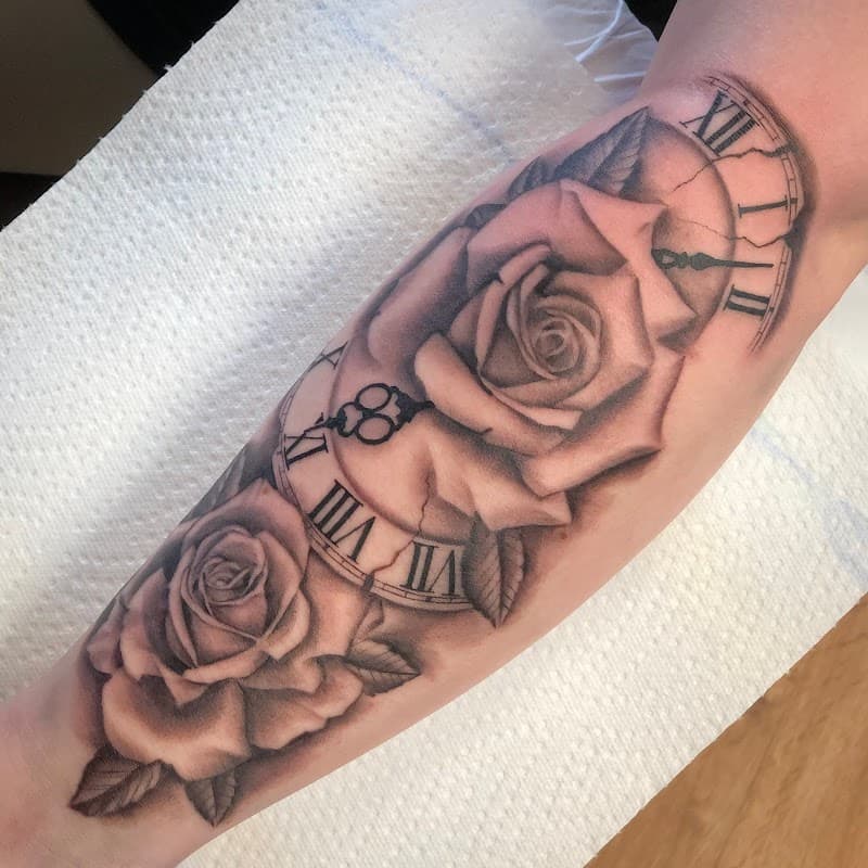 Zwart-wit tattoo van rozen en een klok op de onderarm.