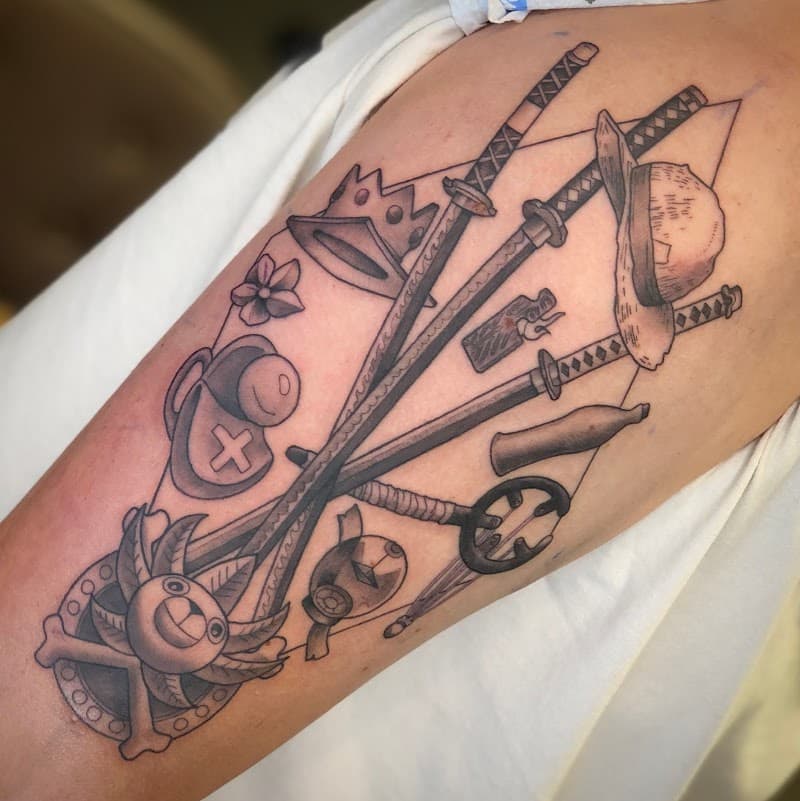 One Piece collage tattoo met zwaarden, hoed en symbolen op bovenarm.