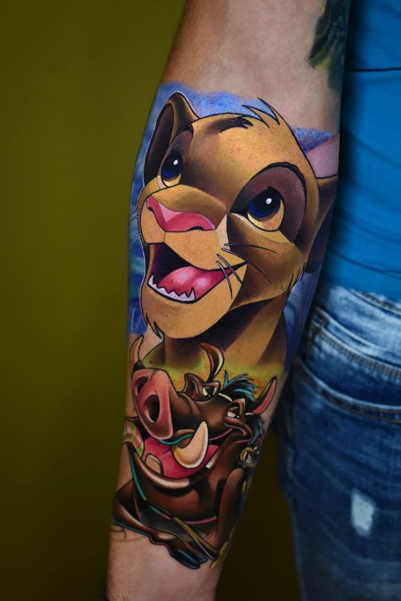 Kleurrijke Lion King tattoo met Simba en Pumbaa op de onderarm.