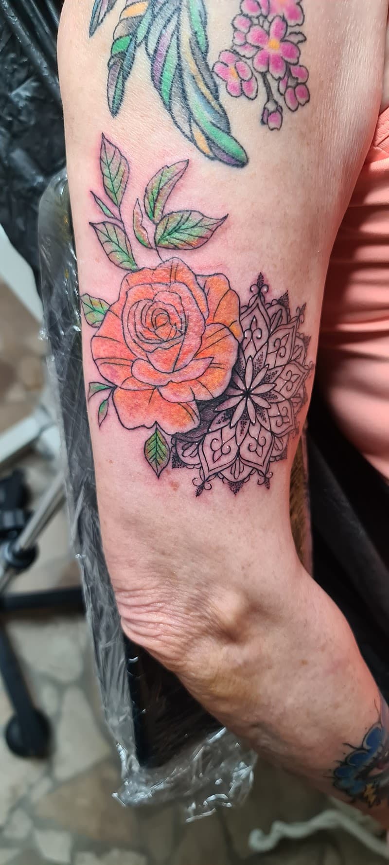 Oranje roos met mandala en kleine bloemen op bovenarm.