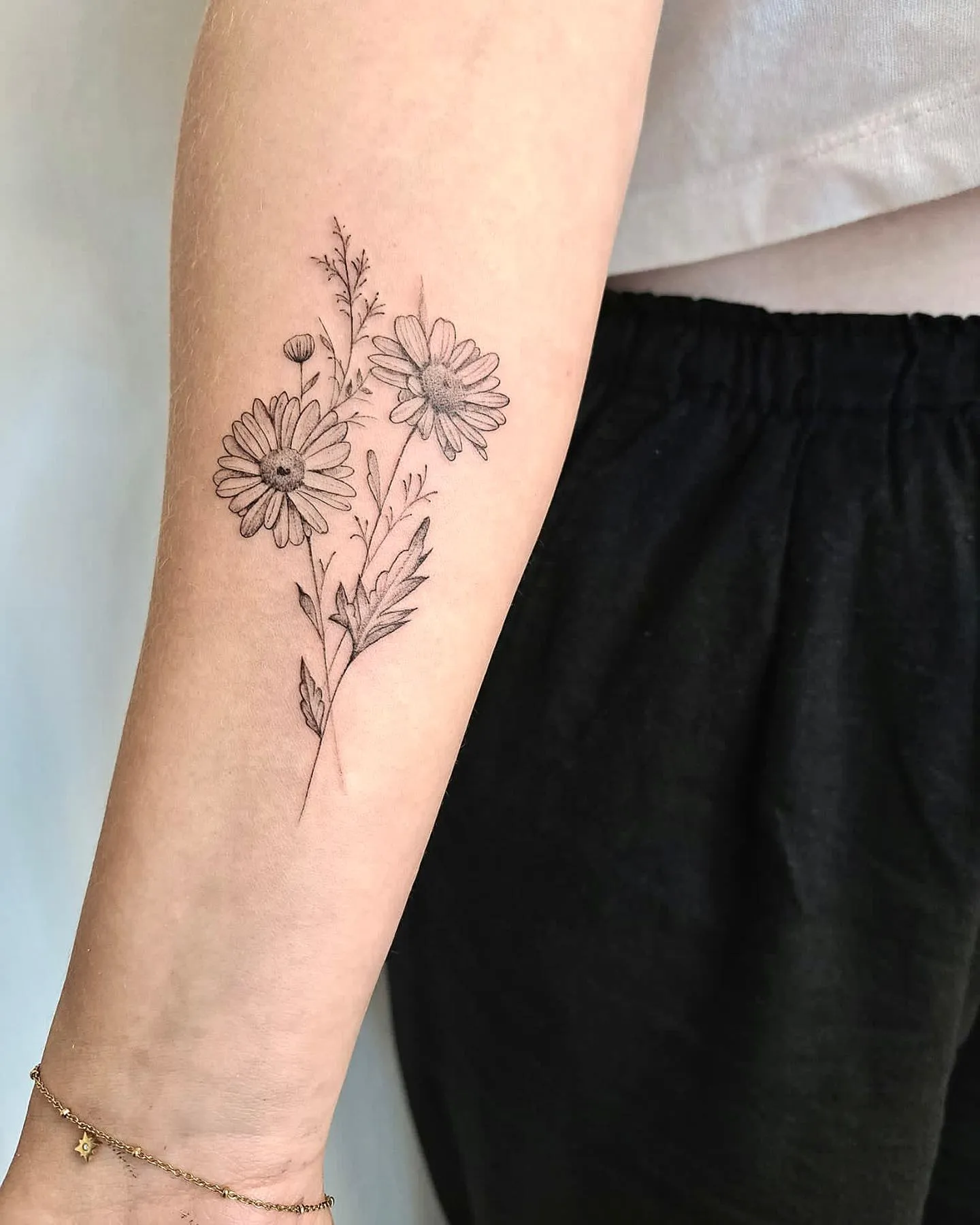 Fineline tattoo van twee madeliefjes en takjes op de onderarm.