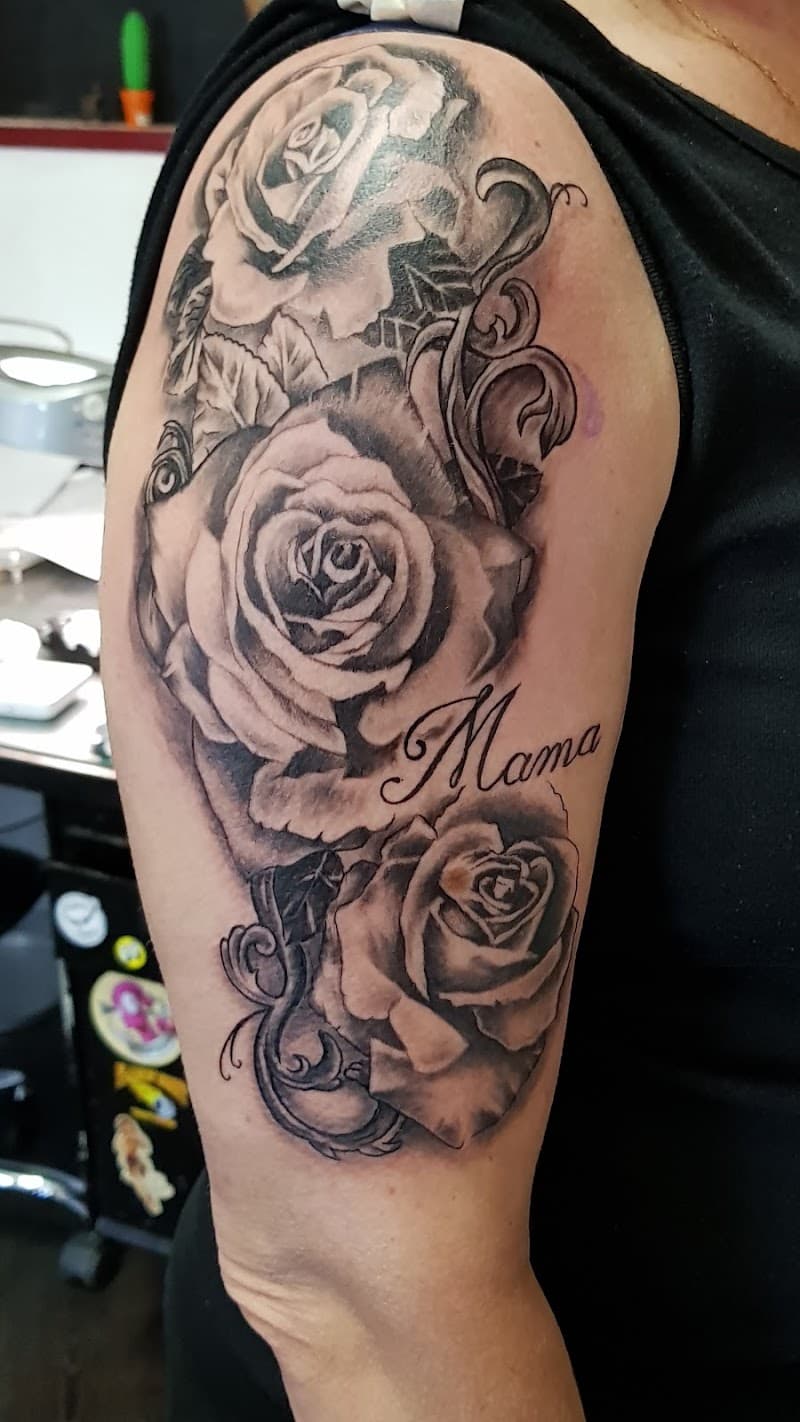 Zwart-grijze rozen met 'Mama' tekst en sierlijke krullen op bovenarm.