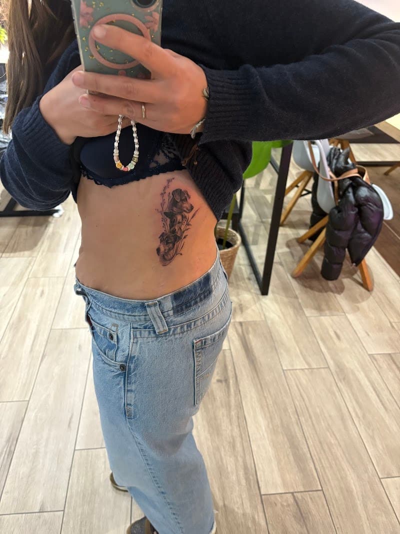 Zwart-wit tattoo van twee hondenkoppen met bloemen op de ribben.