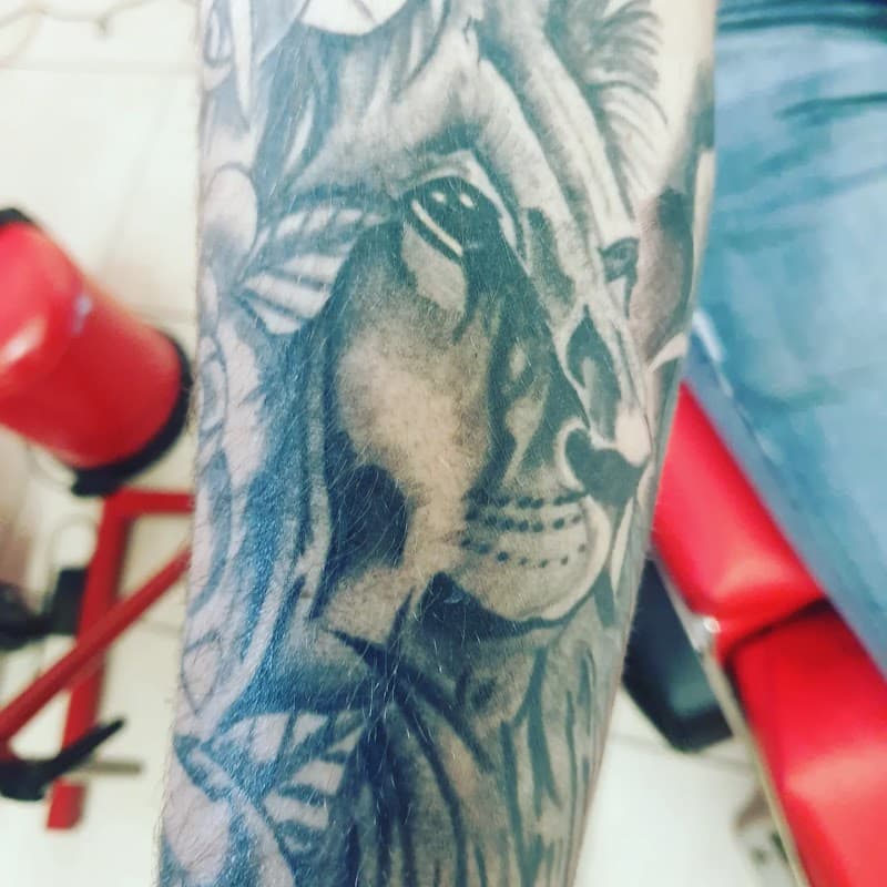 Zwart-wit tattoo van een leeuwenkop op de onderarm.