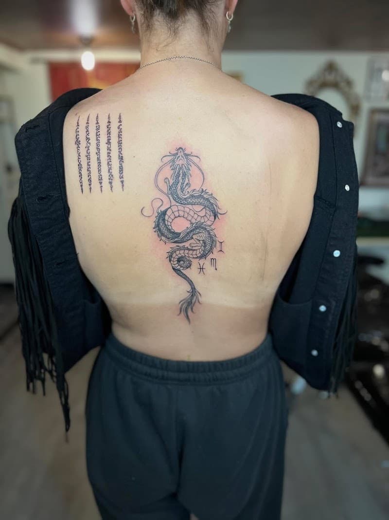 Fineline draak op ruggengraat en Sak Yant script op schouderblad.