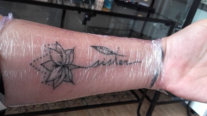 Zwart-wit lotusbloem met 'sister' tekst en pijl op onderarm.