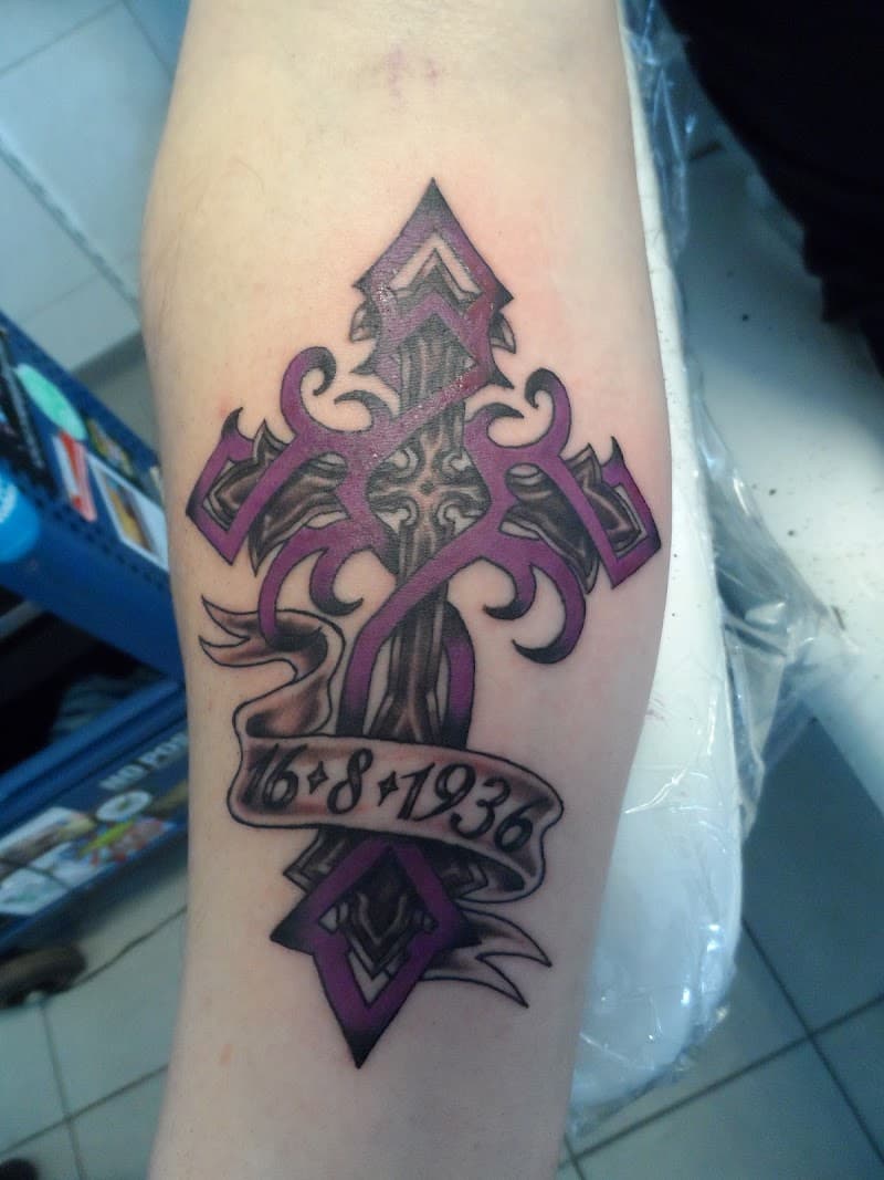 Kruis tattoo met paarse tribal patronen en een banner met de datum 16-8-1936.