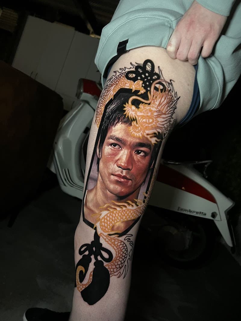 Realistisch portret van Bruce Lee met een gouden draak en zwarte knopen op het bovenbeen.