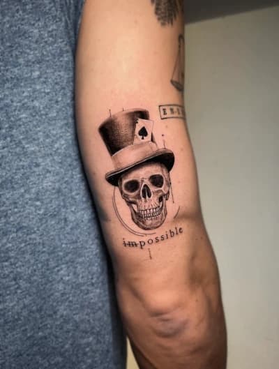 Schedel met hoge hoed, schoppenaas kaart en tekst 'impossible' op bovenarm.
