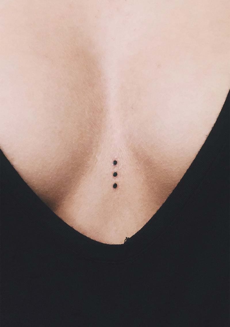 Minimalistische tattoo van drie verticale stippen op het borstbeen.