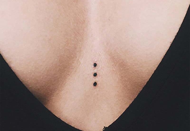Minimalistische tattoo van drie verticale stippen op het borstbeen.