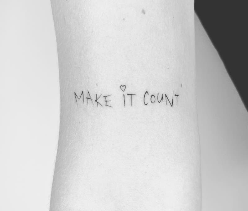 Minimalistische 'MAKE IT COUNT' tekst met hartje op arm.