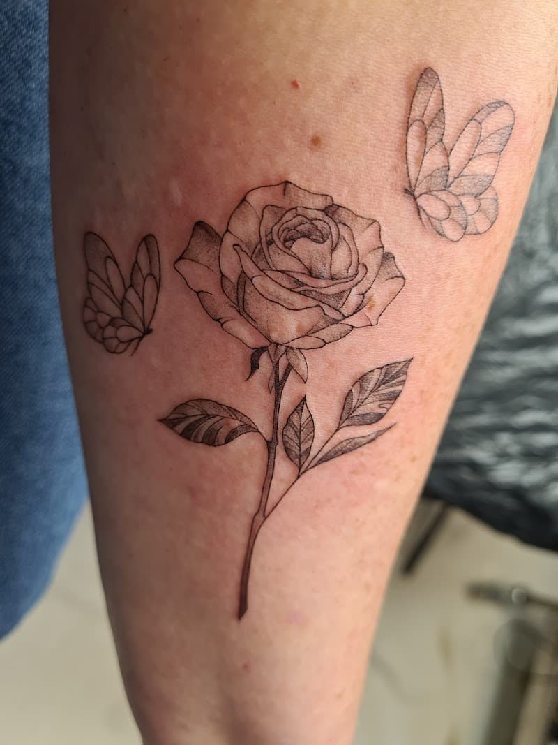 Fineline tattoo van een roos met twee vlinders op de onderarm.
