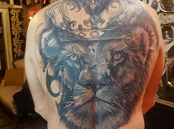 Grote zwart-wit tattoo van een leeuwenkop met een kroon op de rug.