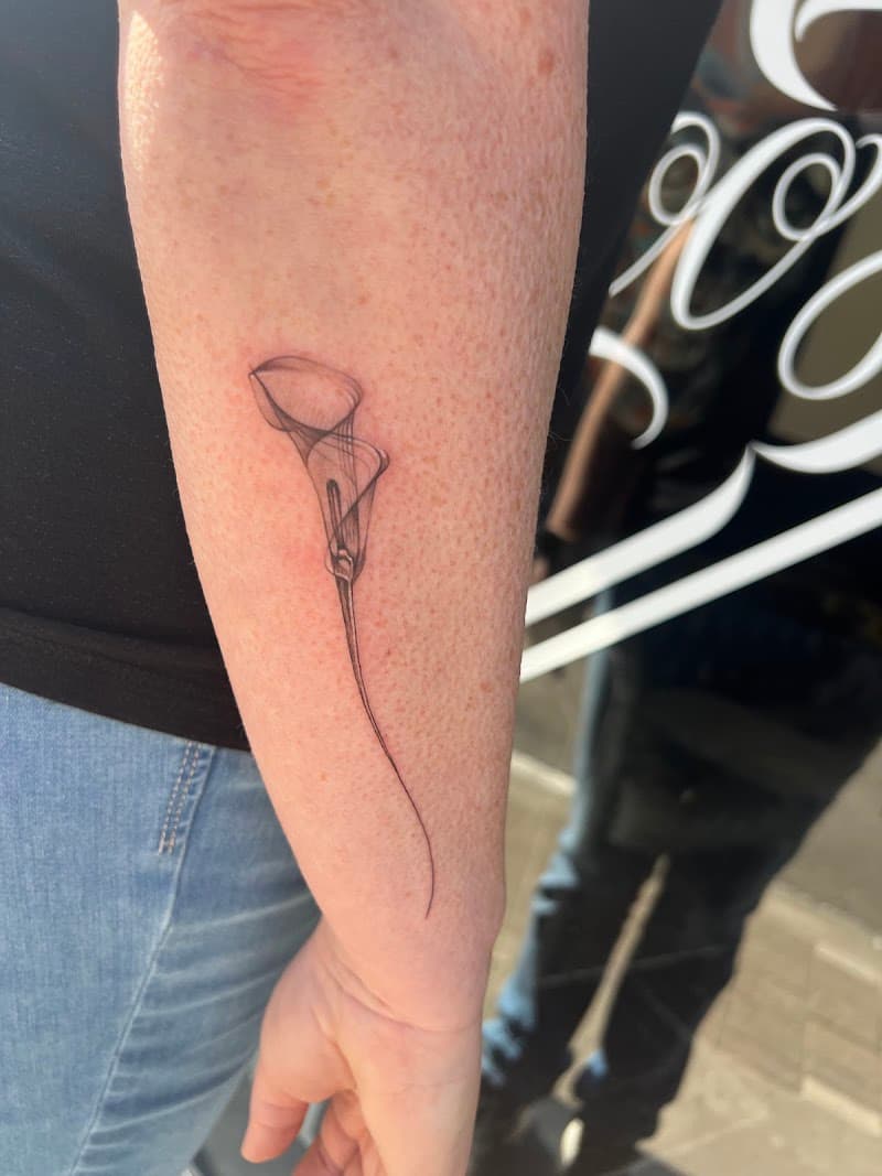 Fijne, transparante calla lelie tattoo op onderarm.