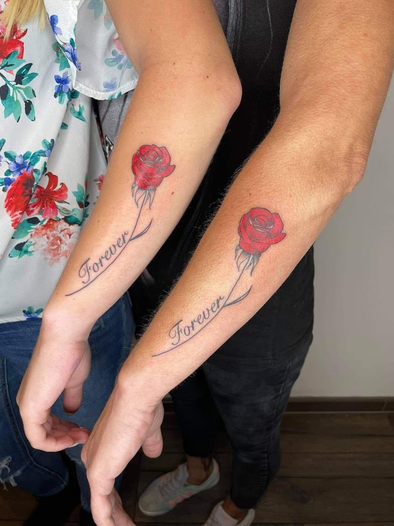 Twee identieke rode roos tattoos met de tekst 'Forever' op onderarmen.