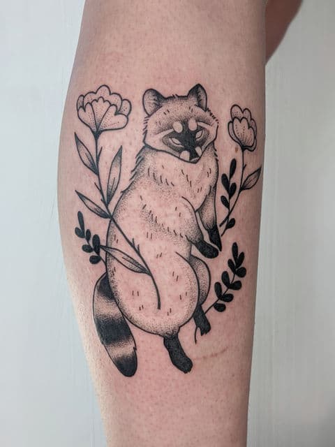 Blackwork tattoo van een tanuki met bloemen op het onderbeen.