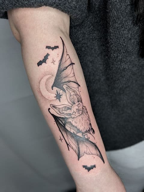 Zwartwerk tattoo van een vleermuis met maan en sterren op de onderarm.