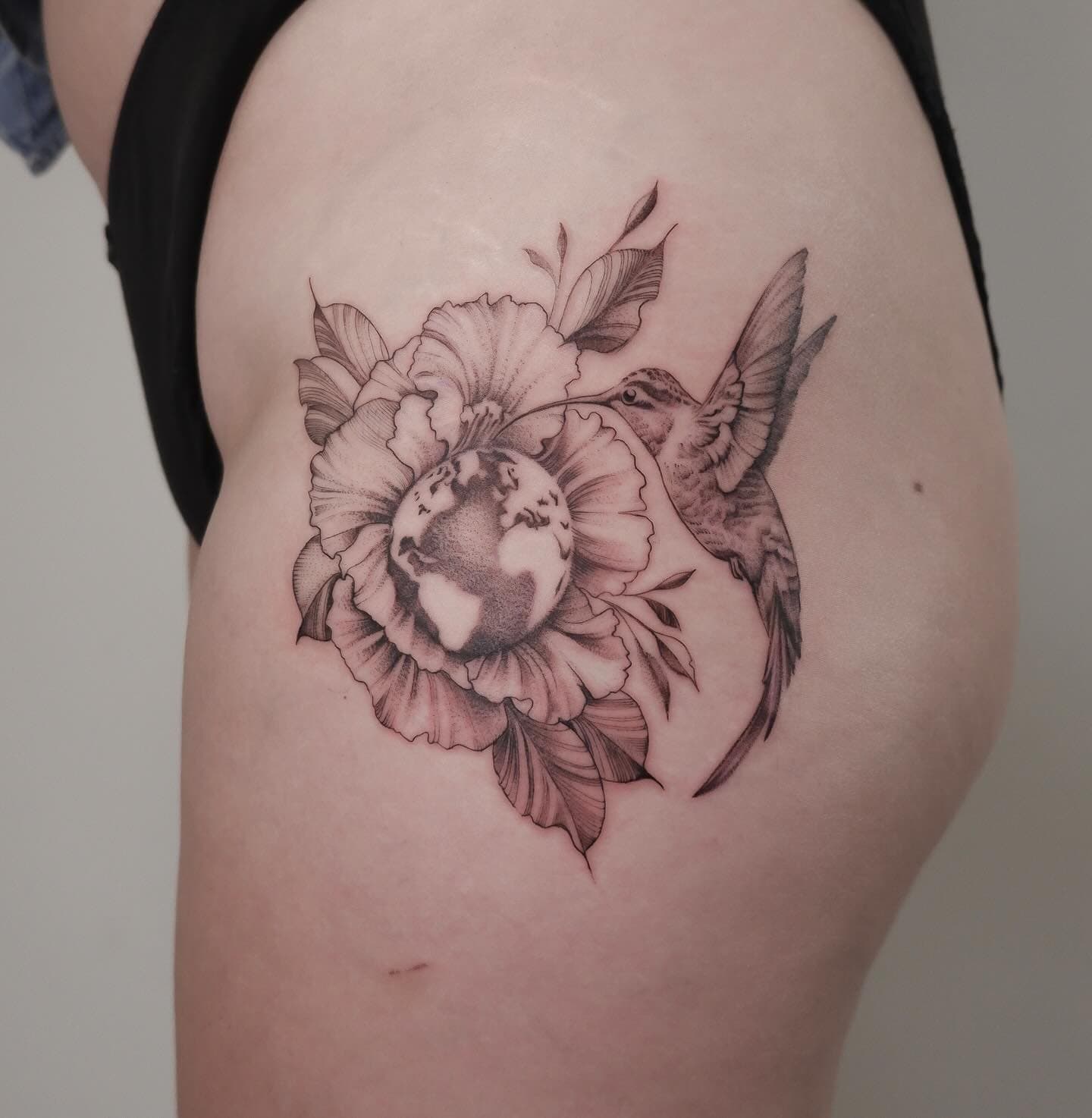 Fineline tattoo van een kolibrie bij een bloem met een wereldbol erin.