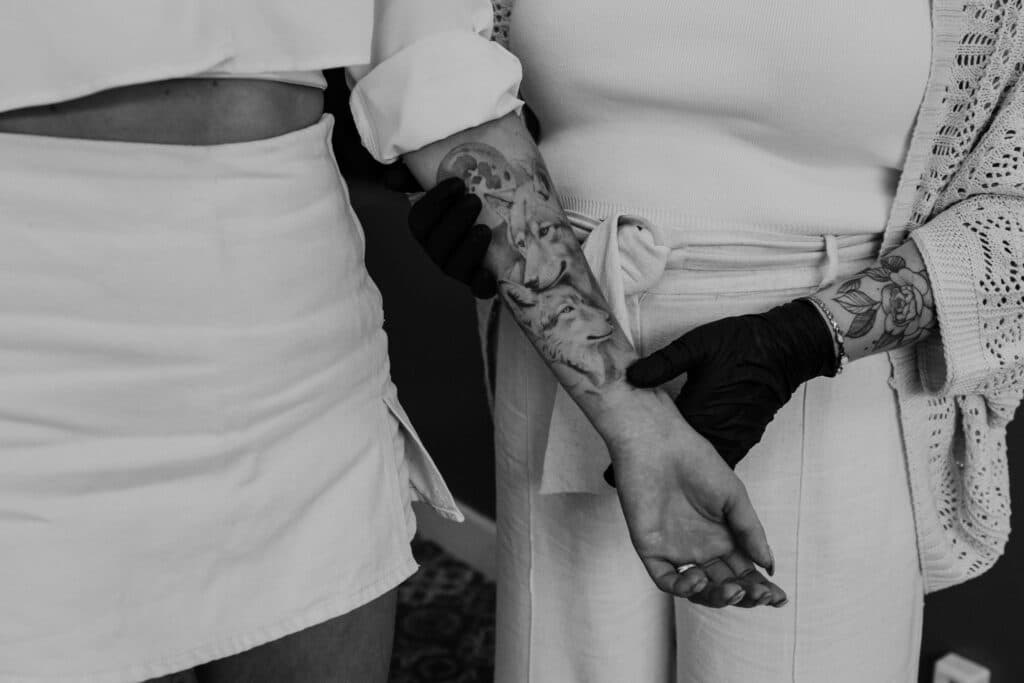 Realistische zwart-wit tattoo van twee wolven en een maan op de onderarm.