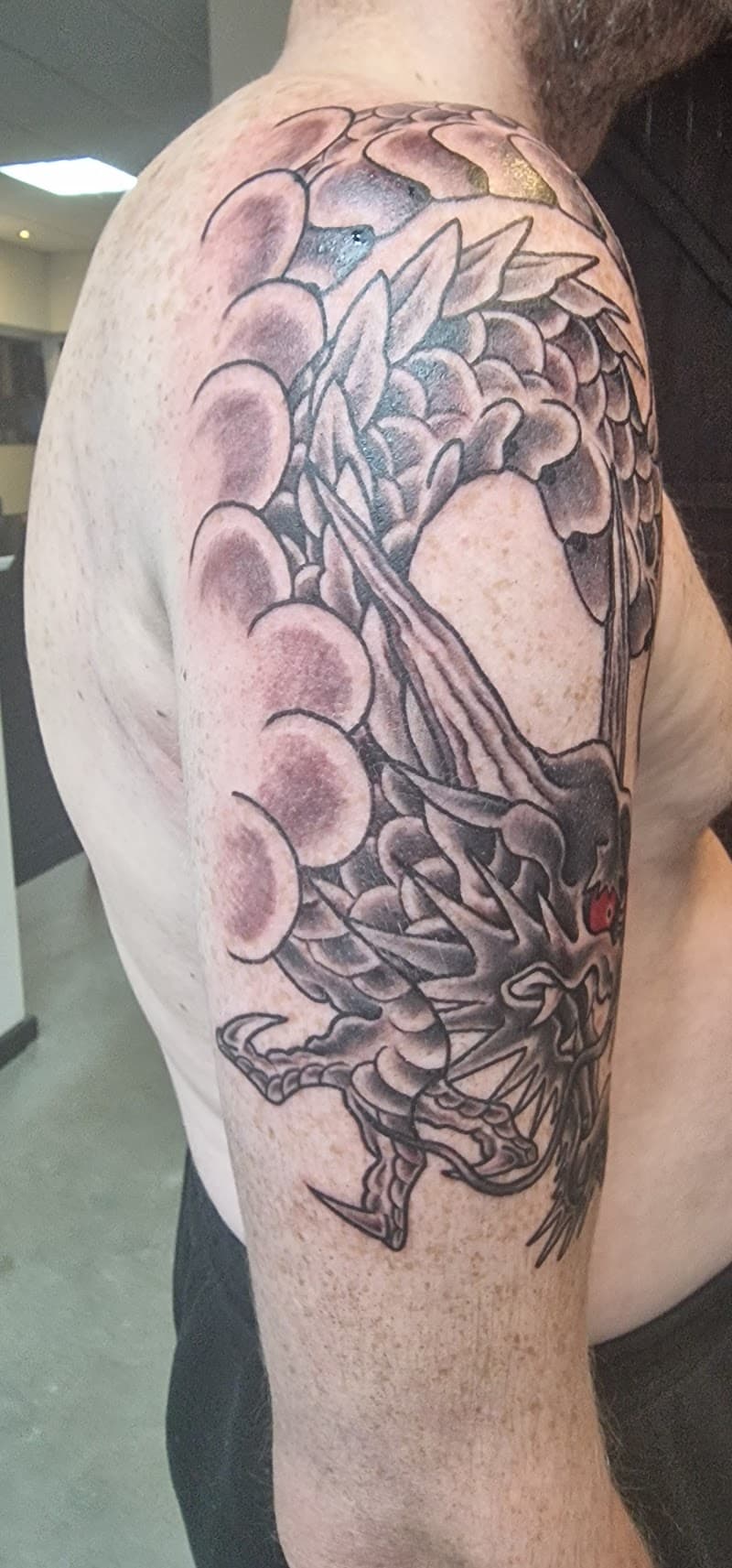 Zwart-grijze draak met rode ogen op bovenarm.