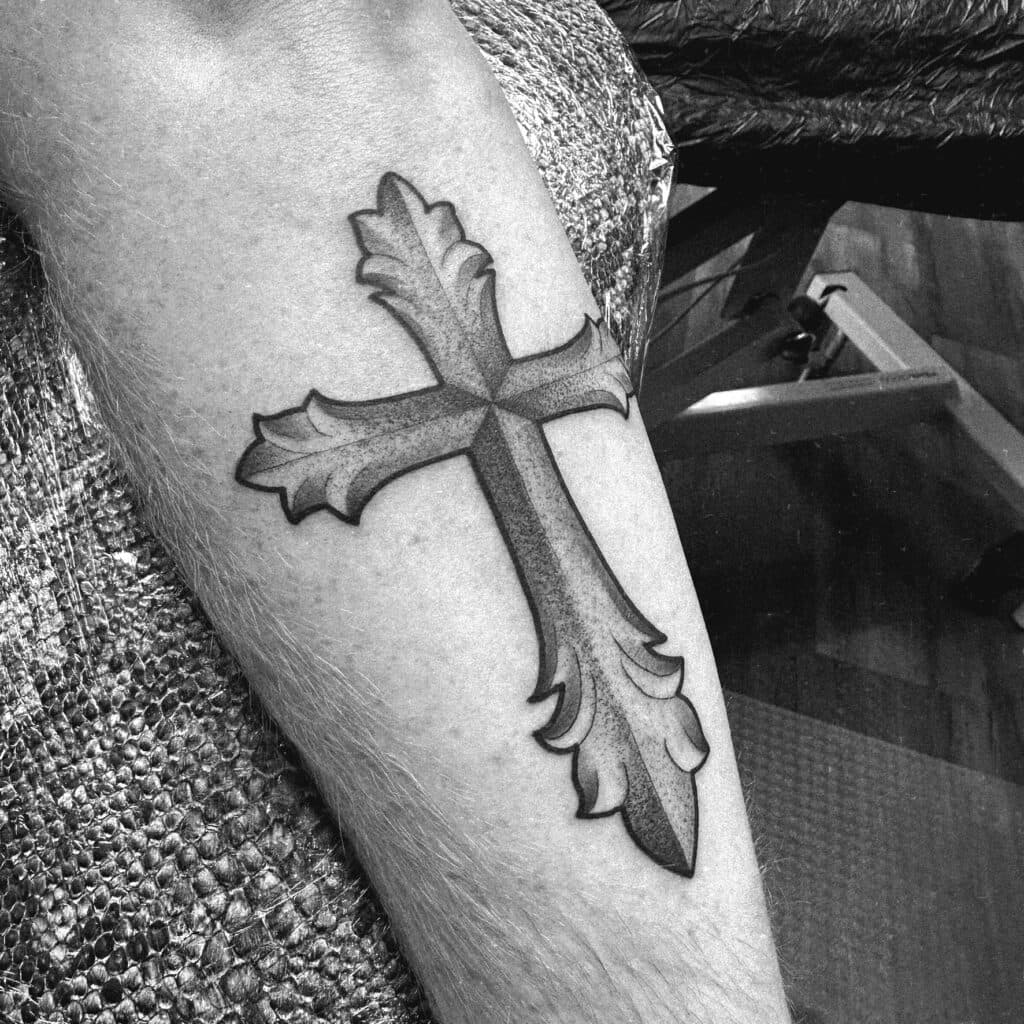 Zwart-wit kruis tattoo met sierlijke, bladvormige uiteinden.