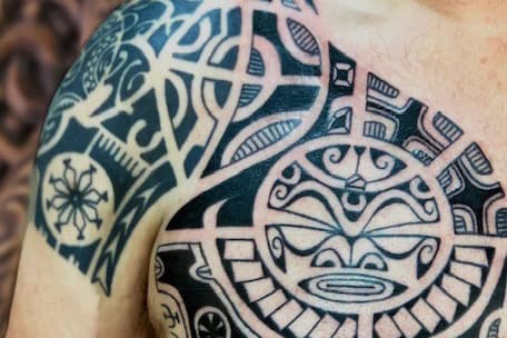 Grote Polynesische tribal tattoo op schouder en borst met tiki gezicht.
