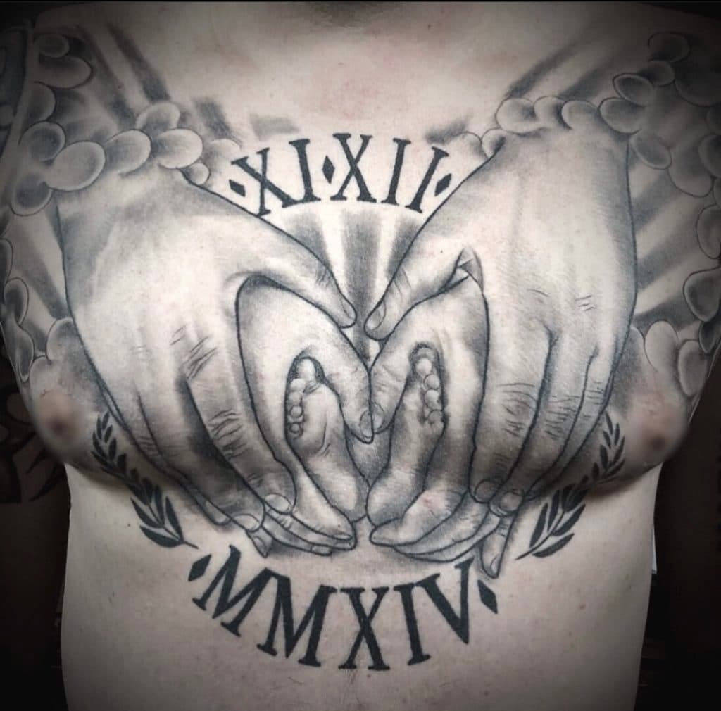 Zwart-wit tattoo van handen die babyvoetjes vasthouden, met Romeinse cijfers.