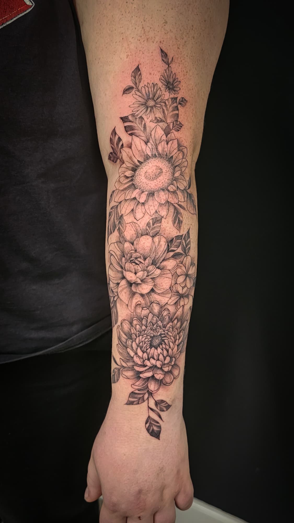 Grote fineline bloemen tattoo op de onderarm met zonnebloem, pioenroos en chrysant.