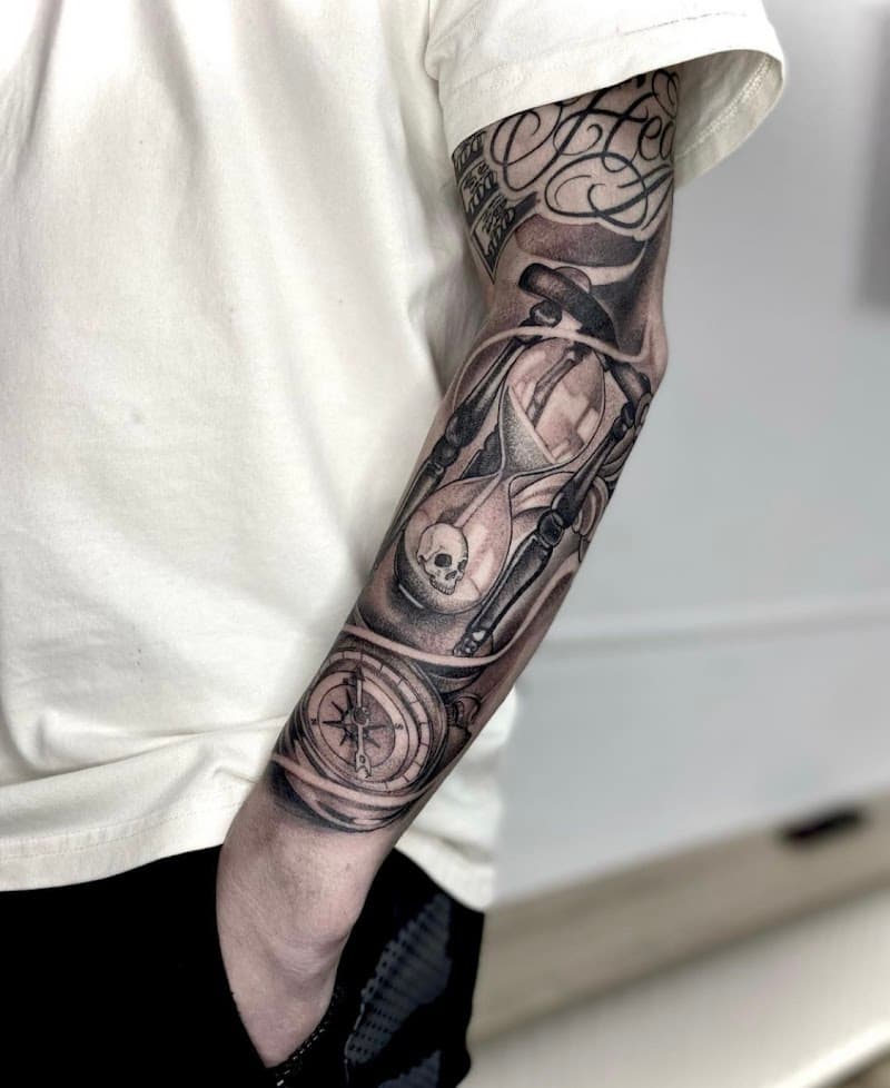 Zwart-wit tattoo van zandloper met schedel en kompas op onderarm.