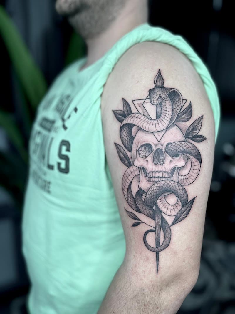Zwart-wit tattoo van een slang die om een schedel en dolk kronkelt, met bladeren.