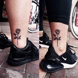 Minimalistische zwarte roos tattoo op de enkel.