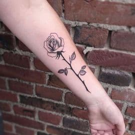 Zwart-wit fineline roos met steel en bladeren op onderarm.