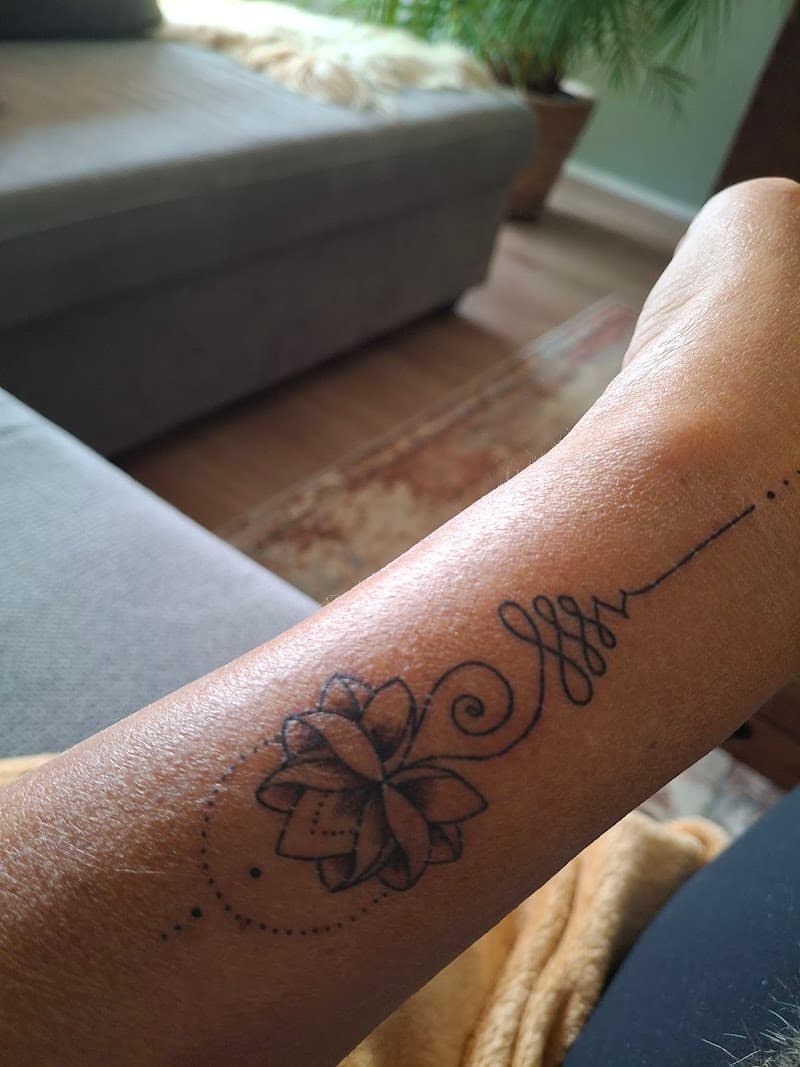 Fineline lotusbloem met unalome symbool op de onderarm.