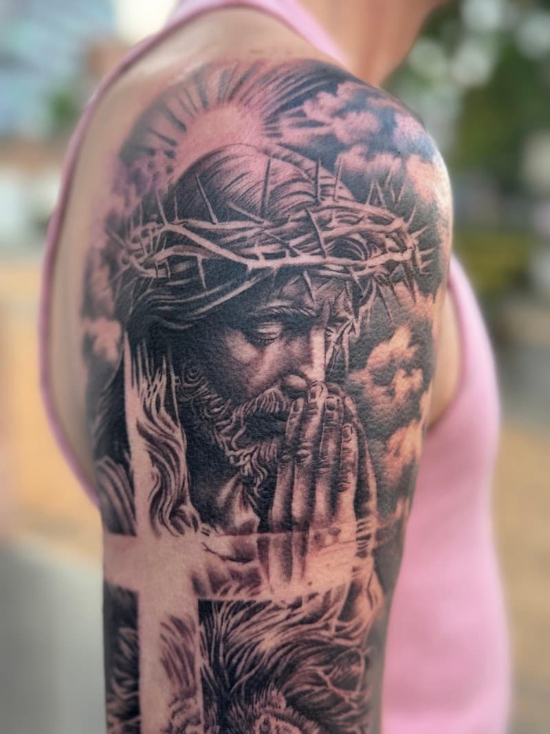 Realistisch portret van biddende Jezus met doornenkroon op bovenarm.