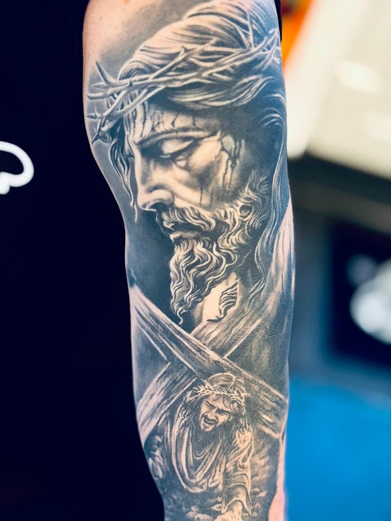 Realistisch portret van Jezus met doornenkroon en kruis op bovenarm.