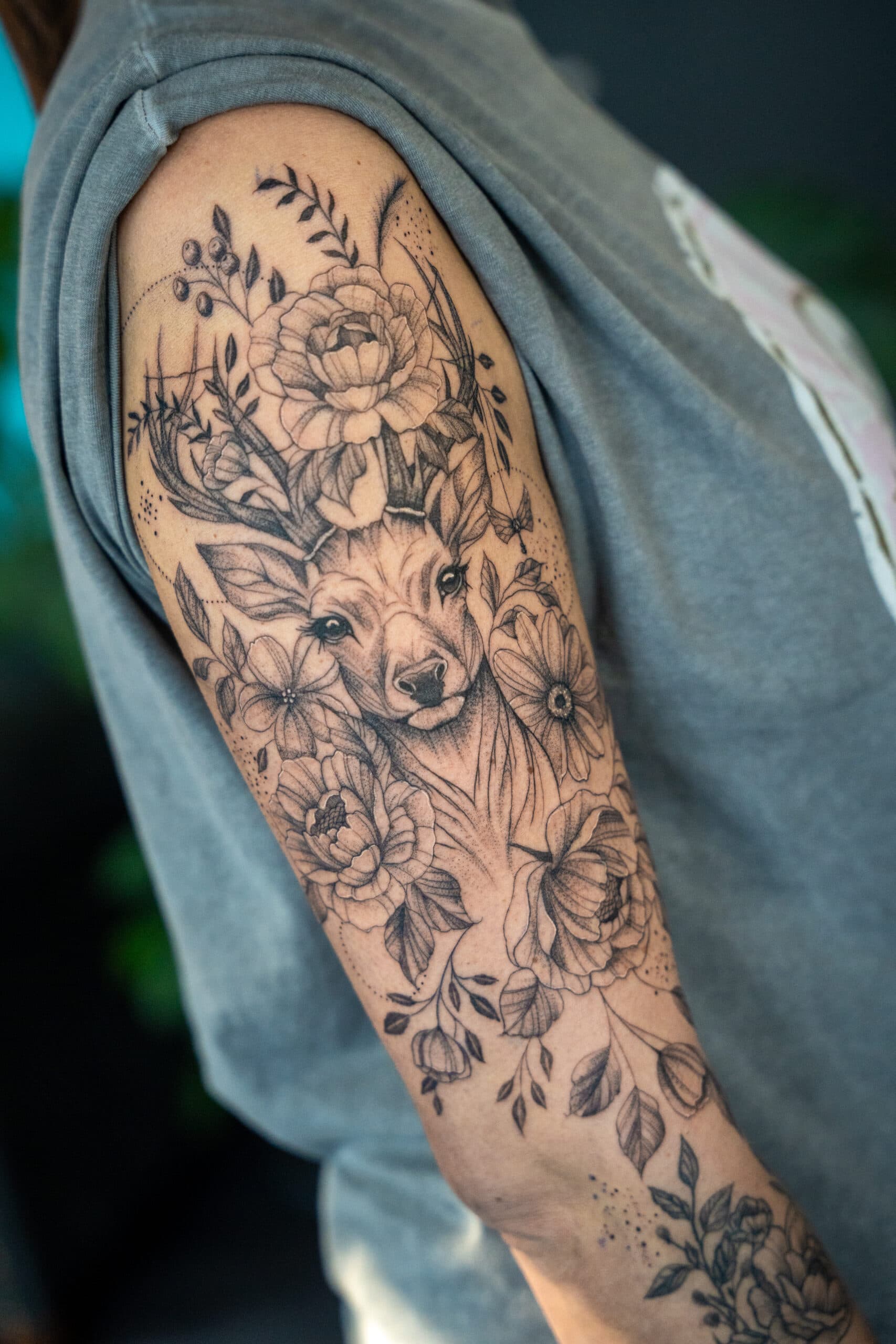 Gedetailleerde hertenkop met bloemen en bladeren op bovenarm.