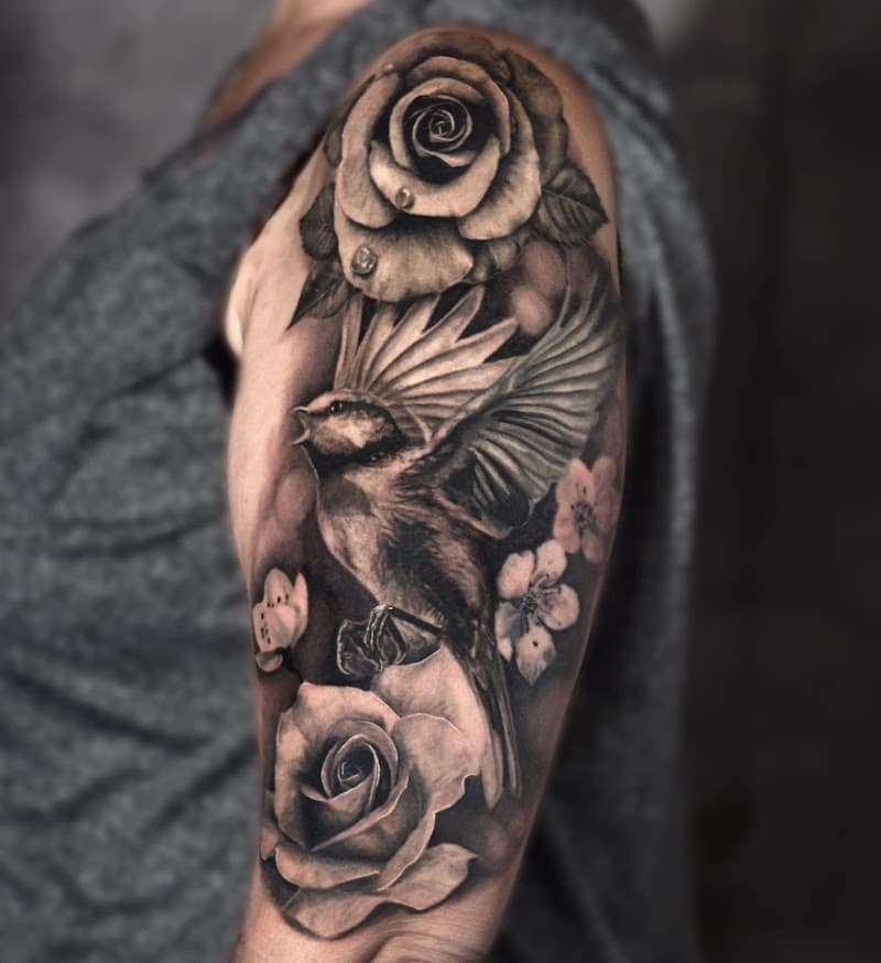Realistische zwart-wit tattoo van een vogel en rozen op de bovenarm.