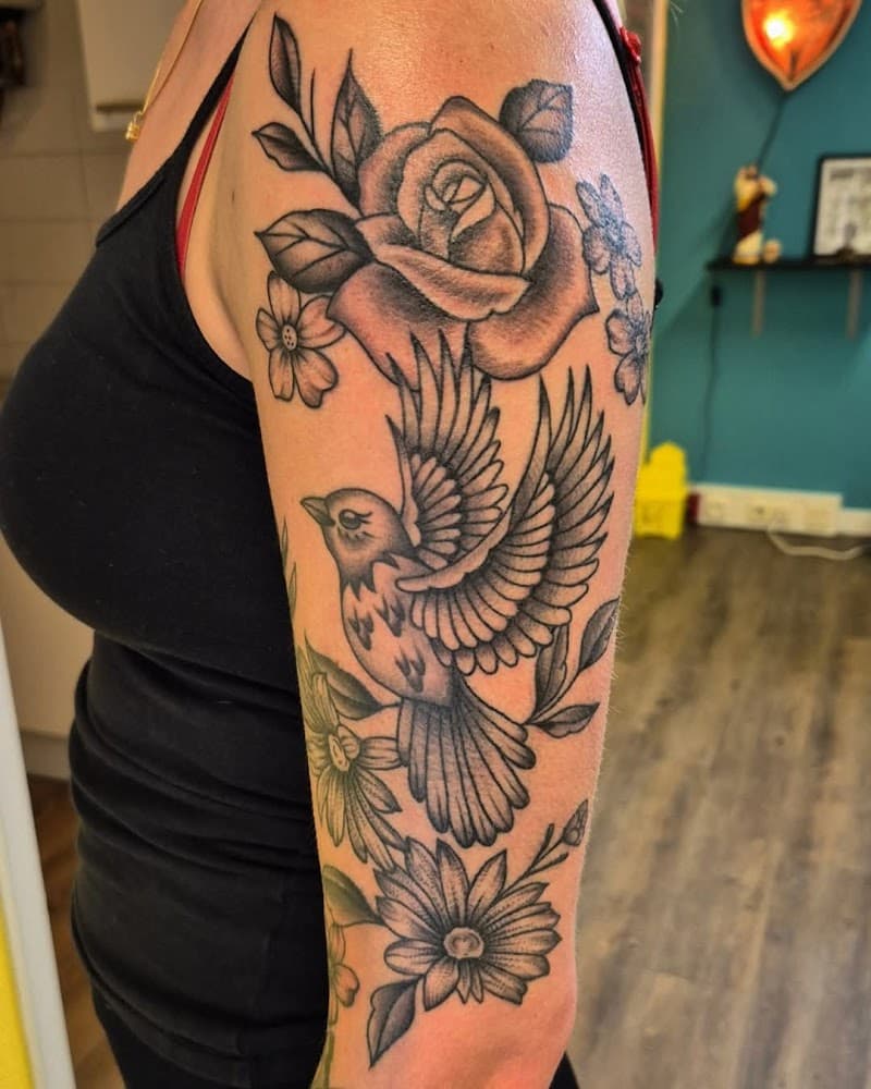 Zwart-wit tattoo van een vogel en bloemen op de bovenarm.
