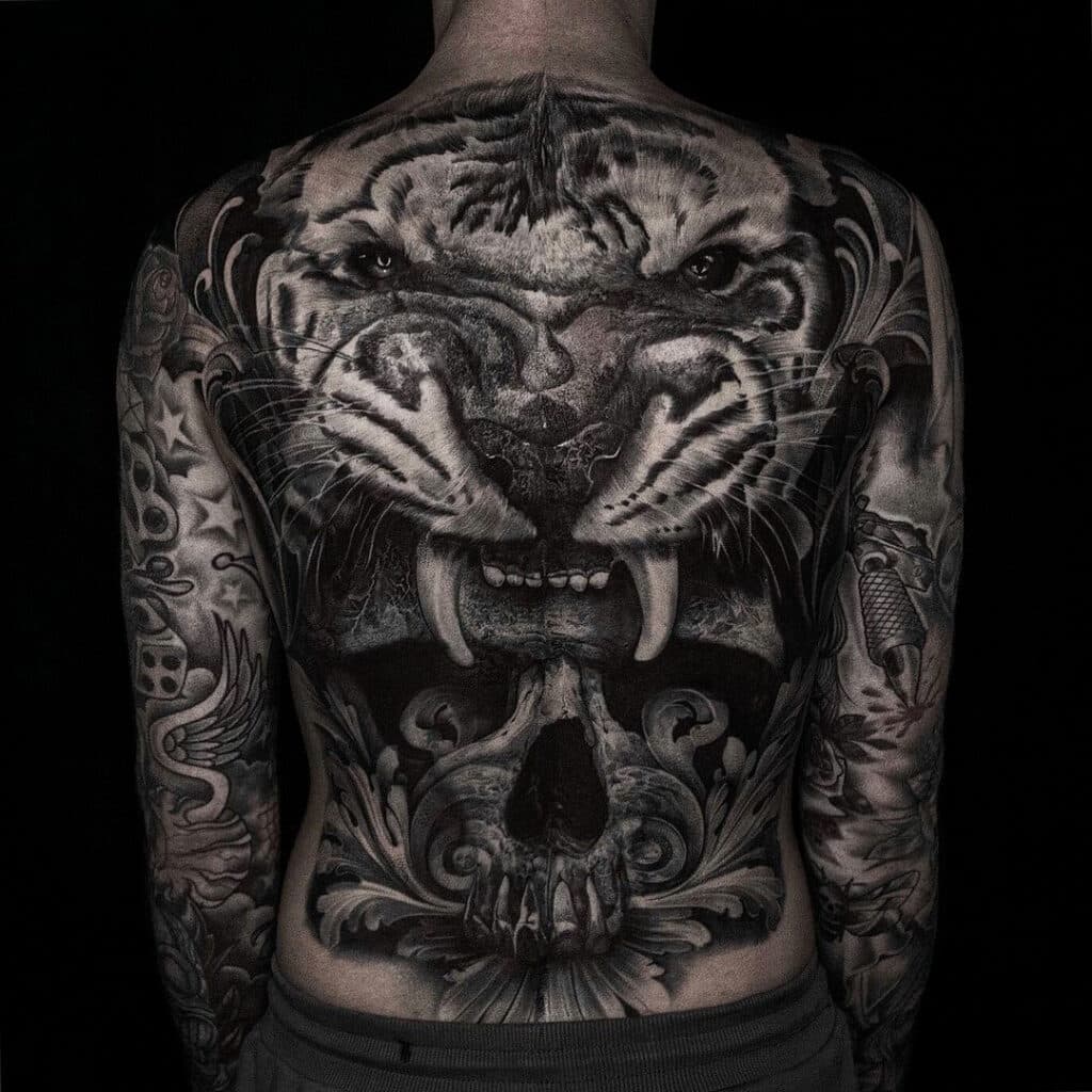 Grote realistische rugtattoo van een brullende tijger, schedel en sierlijke krullen.