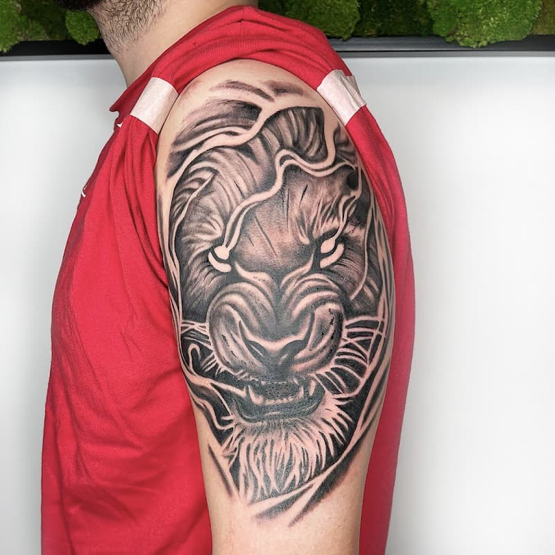 Zwart-wit leeuwenkop tattoo met witte ogen op bovenarm.