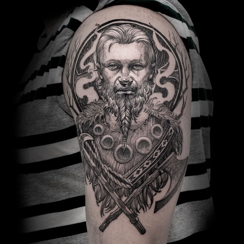 Gedetailleerde zwart-wit tattoo van een Viking krijger met bijlen op de bovenarm.