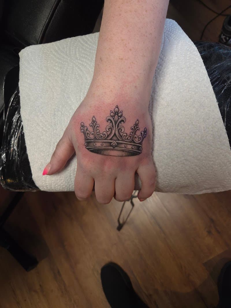 Gedetailleerde zwart-wit kroon tattoo op de bovenkant van de hand.