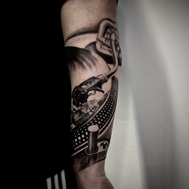 Realistische zwart-wit tattoo van een draaitafel op de onderarm.