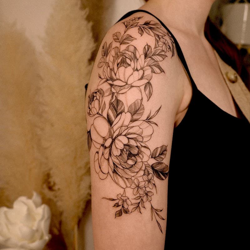 Fineline bloemen tattoo met pioenen op de bovenarm.