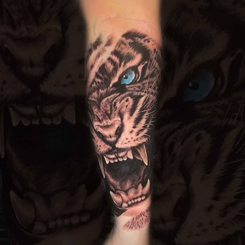 Realistische tijgerkop met blauwe ogen en open bek op onderbeen.